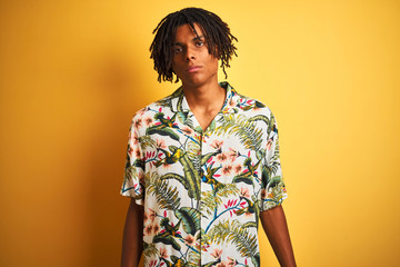 Afro man with dreadlocks on vacation wearing summer shirt over isolated yellow background Relaxed with serious expression on face. Simple and natural looking at the camera.