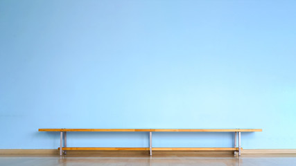 wooden bench stands on parquet floor in empty room with blue concrete wall