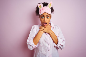 Young african american woman wearing pajama and mask over isolated pink background shouting suffocate because painful strangle. Health problem. Asphyxiate and suicide concept.