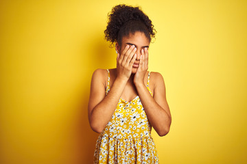 African american woman wearing casual floral dress standing over isolated yellow background rubbing eyes for fatigue and headache, sleepy and tired expression. Vision problem