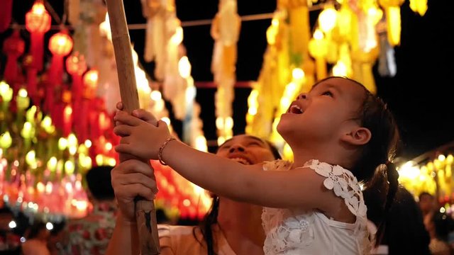 Happy Asian family hanging a thai lanna lantern to make a wish in Yi Peng Festival at the Cham Devi courtyard, Lamphun province. 
