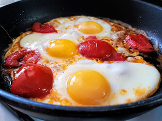 Fried eggs with ripe red cut tomatoes. Dish in a frying pan, top view