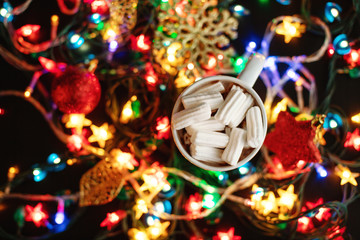 Fototapeta na wymiar Cup of homemade hot chocolate with white marshmallows, a lot of lights of stars garland and christmas tree ornament, christmas and new year concept