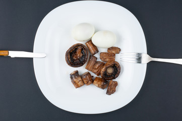 Mushrooms and boiled eggs on a white plate isolated on a black background.Natural food