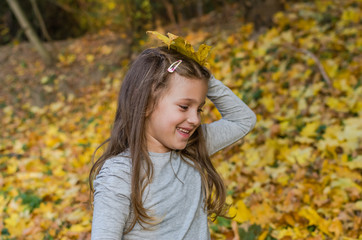 Little charming girl child throws up fallen yellow maple leaves in autumn park