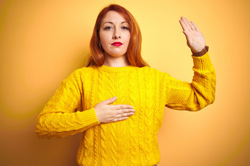 Beautiful redhead woman wearing winter sweater standing over isolated yellow background Swearing...