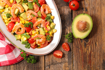vegetable salad with shrimp, tomato, avocado and corn- top view on wood background