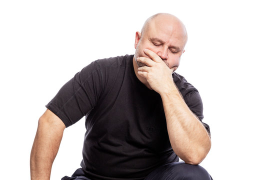 A serious bald middle-aged man in a black T-shirt is sitting with his hand in his face. Isolated over white background. - Powered by Adobe