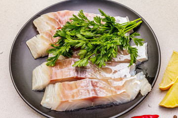 Raw pollock (Pollachius virens) pieces. Fresh fish for healthy food lifestyle. Lemon, parsley, sea salt, chili, black peppercorn