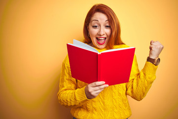 Young redhead teacher woman reading red book over yellow isolated background screaming proud and celebrating victory and success very excited, cheering emotion