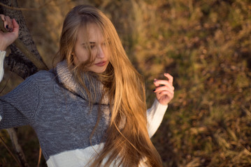 Beautiful elegant woman in a park. She's lying on a tree trunk. She has long Golden hair. autumn.