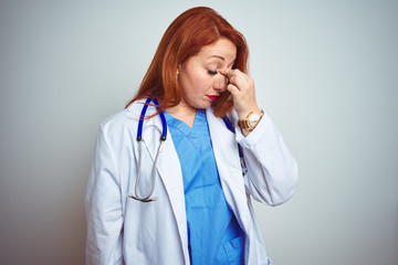 Young redhead doctor woman using stethoscope over white isolated background tired rubbing nose and...