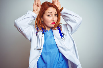 Young redhead doctor woman using stethoscope over white isolated background Doing bunny ears...
