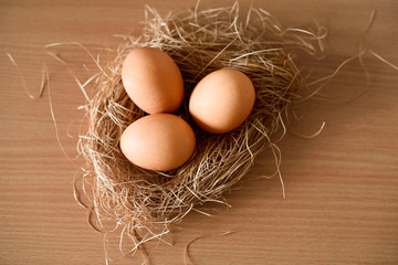Three chicken eggs lie in a nest on a wooden table
