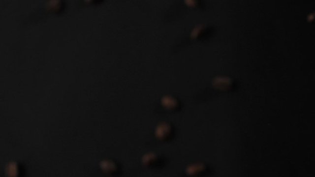 Roasted coffee beans fly after being exploded on black background. Fragrant fresh flying coffee beans. Slow Motion.