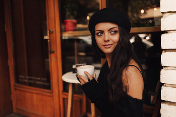 beautiful young curly woman in hat with cup of coffee in cafe