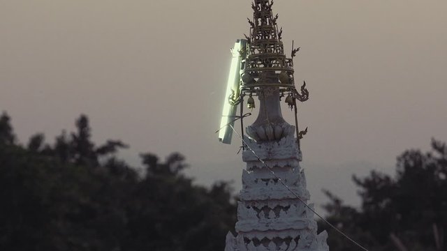 Lamp on Burmese hti ornament turns on atop ornate pagoda in Myanmar to illuminate night.