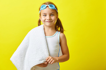 Beautiful little girl in swimsuit and swimming glasses standing on yellow isolated background.