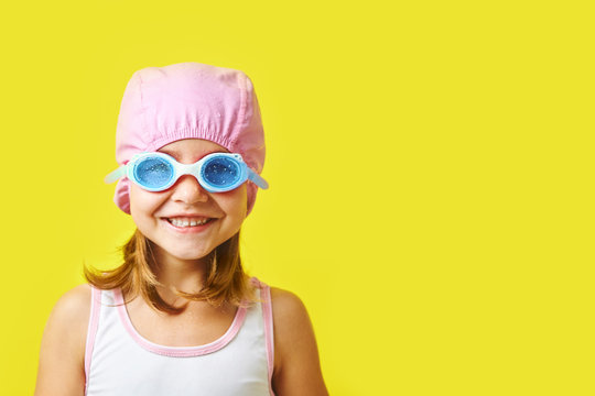 Smiling little girl in swimming cap and glasses on colored background with free copyspace.