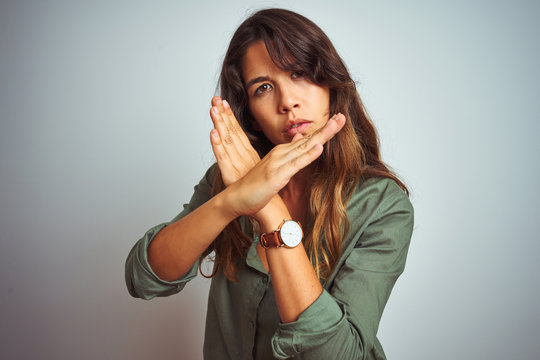Young beautiful woman wearing green shirt standing over grey isolated background Rejection expression crossing arms doing negative sign, angry face