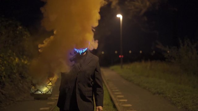 Man with purge mask and burning and smoking lantern is standing on a railway at night.