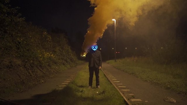 Man with purge mask and burning and smoking lantern is standing on a railway at night.