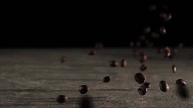 Roasted coffee beans falling down on ceramic background. Fragrant fresh falling coffee beans. Slow Motion.