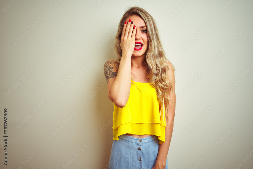 Wall mural young beautiful woman wearing yellow t-shirt standing over white isolated background covering one ey