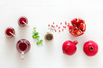 Pomegranates and chia seeds with fresh mint. A glass pitcher of fresh red juice with two full jars. An inviting fresh drink on a clean white table background.