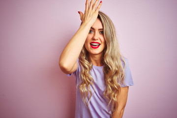 Young beautiful woman wearing purple t-shirt standing over pink isolated background surprised with hand on head for mistake, remember error. Forgot, bad memory concept.