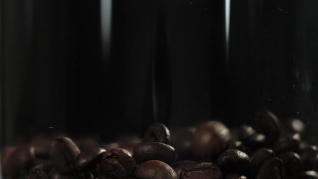 Roasted coffee beans falling down in transparent jar on black background. Fragrant fresh falling coffee beans. Slow Motion.