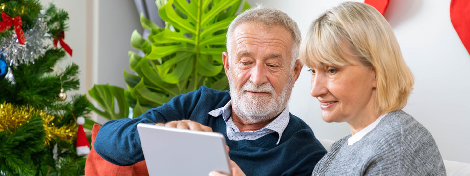 Senior couple using tablet to video phone call to greeting their family for Christmas festival, sitting on sofa with decoration and tree - Powered by Adobe