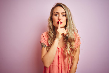 Young beautiful woman wearing t-shirt standing over pink isolated background asking to be quiet with finger on lips. Silence and secret concept.