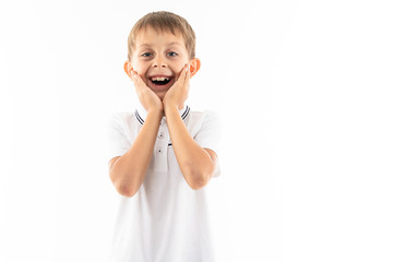 A little boy in a white shirt, blue shorts with blonde hair stands and is smiling