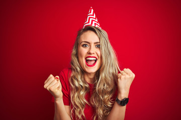 Young beautiful woman wearing bitrhday hat over red isolated background screaming proud and celebrating victory and success very excited, cheering emotion