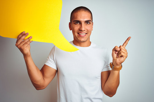 Young man holding yellow speech bubble over white isolated background very happy pointing with hand and finger to the side
