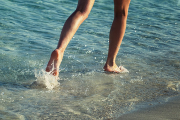 Woman is running ahead on beach of sea. Legs close-up