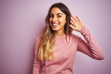 Fototapeta premium Young beautiful woman wearing a sweater over pink isolated background smiling with hand over ear listening an hearing to rumor or gossip. Deafness concept.