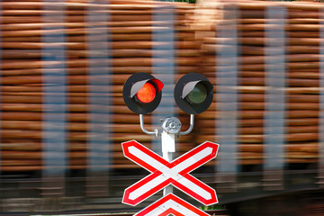 Freight train with a load of logs passing a railway crossing at high speed. Red light at railway...