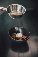 Chef making Miso Ramen Asian noodles with egg, enoki and pak choi cabbage in bowl on dark wooden background background