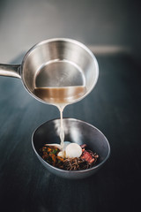 Chef making Miso Ramen Asian noodles with egg, enoki and pak choi cabbage in bowl on dark wooden background background