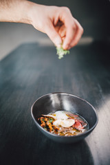 Chef making Miso Ramen Asian noodles with egg, enoki and pak choi cabbage in bowl on dark wooden background background