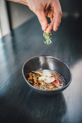 Chef making Miso Ramen Asian noodles with egg, enoki and pak choi cabbage in bowl on dark wooden background background