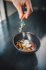 Chef making Miso Ramen Asian noodles with egg, enoki and pak choi cabbage in bowl on dark wooden background background