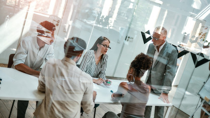 Morning meeting. Group of business people discussing something while sitting at the office table behind the glass wall in the modern office