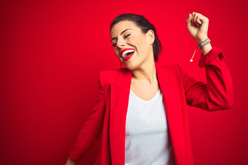 Young beautiful business woman standing over red isolated background Dancing happy and cheerful,...