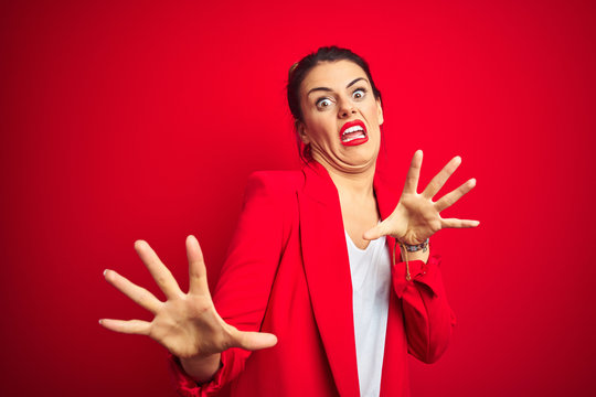 Young beautiful business woman standing over red isolated background afraid and terrified with fear expression stop gesture with hands, shouting in shock. Panic concept.