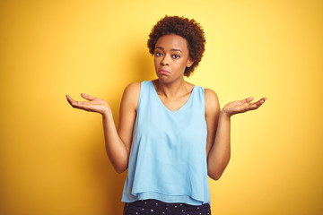 Beautiful african american woman wearing elegant shirt over isolated yellow background clueless and...
