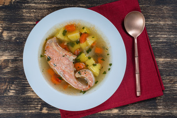 Fresh salmon fish soup with carrots and potatoes in a white plate, close up