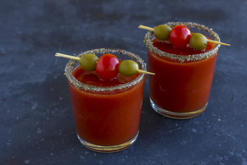 Spicy Vodka Bloody Mary cocktails served with pickled veggies (tomatos, olive and celery) on a dark background.